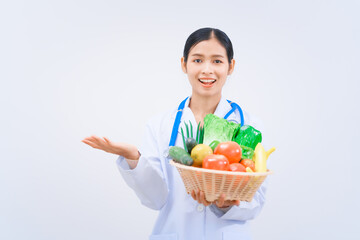 A young Asian woman nutritionist in a white lab coat, holding fruit and vegetable basket, smiling...