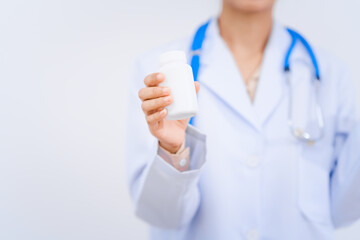 Fototapeta premium A young Asian nutritionist and doctor, smiling happily while wearing a stethoscope and white lab coat. Holding a pill bottle, importance of vitamins, minerals, and balanced nutrition for health.