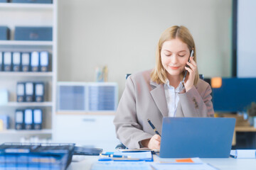 Obraz premium A young Russian woman in formal suit works diligently in business office, analyzing financial charts, using a desktop PC, calculator while contributing to various business strategies and projects.