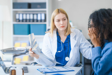 Obraz premium A young African American patient consults with a young Russian medical doctor about her immune system and vitamin intake. They discuss patient medical history, vitamin and pill bottles on the desk.