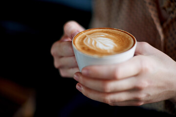Person, hands or cup with coffee at shop for beverage or morning breakfast at indoor restaurant. Closeup, customer or mug with latte, cappuccino or espresso for warm drink, leaf or mocha java at cafe