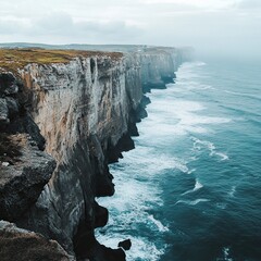 Dramatic coastal cliffs meet turbulent ocean waves under a cloudy sky.