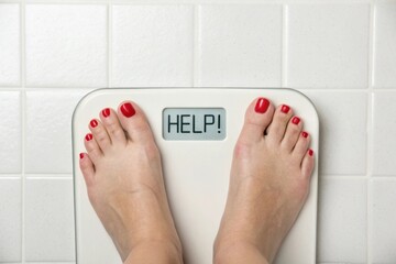 A woman's feet on a bathroom scale displaying "HELP!" in a close-up shot, conveying the emotional weight of a weight-loss struggle.