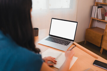 Fototapeta premium woman working at desk with laptop, notebook, and pen in cozy home office setting