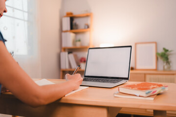 Fototapeta premium person writing in notebook at wooden desk with laptop and books in cozy home office setting
