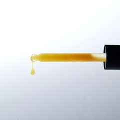 A dropper slowly releases a translucent amber liquid, emphasizing its thickness and smooth consistency against a soft backdrop