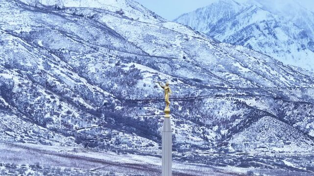 Aerial LDS Temple spire Angel Moroni mountain winter Utah circle. The Church of Jesus Christ of Latter-day Saints, LDS Mormon religion. Sacred building for eternal worship. Residential neighborhood.