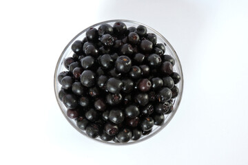 Fresh aronia berries in a glass bowl, white background, top view