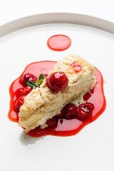 Savor the taste of a luscious napoleon cake elegantly plated with a vibrant cherry sauce and...