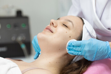 Fototapeta premium woman is getting her face cleaned with a cloth. The woman is wearing a white headband and blue gloves