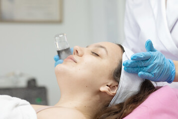 Naklejka premium woman is getting her face done by a beautician. The beautician is holding a bottle of black liquid and a device. 