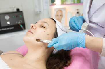 Naklejka premium Close-up portrait of a beautiful woman with closed eyes and apparatus for skin rejuvenation. Beauty salon procedures. RF lifting. Microcurrents.