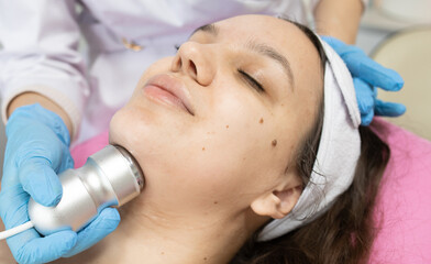 Woman is getting a facial treatment with a RF lifting device on her face. The woman is wearing a white bandana and a blue glove