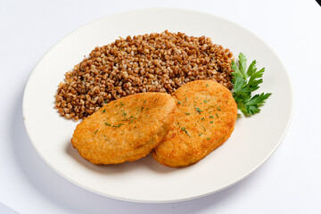 Two golden-brown breaded cutlets rest on a plate next to a generous serving of fluffy buckwheat, accented with a sprinkle of fresh parsley for color and flavor. 