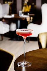 A beautifully crafted cocktail sits on a polished wooden table in an upscale lounge. Soft lighting enhances the atmosphere, making it a perfect setting for relaxation and indulgence. 