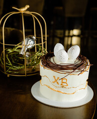 This festive Easter cake features a smooth white frosting, chocolate eggs nestled on top, and a charming birdcage in the background, embodying the joy of the spring season. 