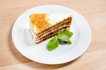 A tempting slice of layered cake, featuring rich cream and crumbly texture, rests on a white plate. Fresh mint leaves add a refreshing touch, perfect for dessert time. 
