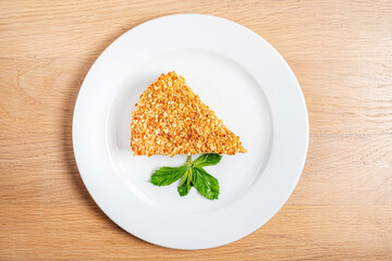 This delectable slice showcases a crunchy nutty exterior, perfectly shaped and adorned with a sprig of fresh mint. It invites sweet indulgence, set against the calming backdrop of a wooden table.