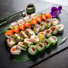 A stunning assortment of sushi rolls showcases vibrant colors and textures, carefully arranged on a black slate serving board. 