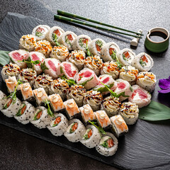 Delight in a beautiful assortment of sushi rolls meticulously arranged on a dark stone platter....