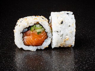 Delicate sushi rolls reveal layers of vibrant salmon and crisp cucumber, artistically arranged on a smooth black surface. The sesame seeds add a delightful touch to this culinary masterpiece. 