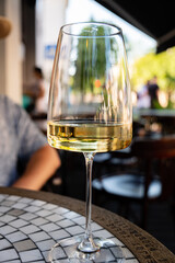 Sunlight glints off a half-full glass of white wine placed on a mosaic table. The vibrant...