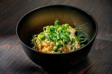 Delicate strands of pasta are beautifully served in a sleek black bowl, topped with fresh green peas and sprigs of herbs, creating an inviting presentation perfect for a gourmet dining experience. 