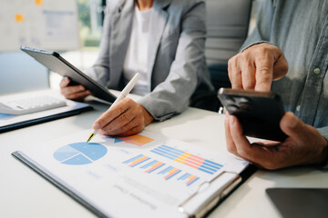 Fototapeta premium Business documents on office table with smart phone and laptop and two colleagues discussing data