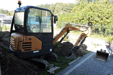 A black and yellow compact hydraulic excavator standing in a courtyard next to heap of dirt