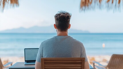 Fototapeta premium A person works on a laptop at a beachside location, overlooking the ocean, embodying a relaxed, remote working lifestyle.