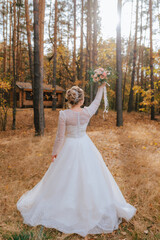 Fototapeta premium a bride in a white dress in an autumn forest with a bouquet in the air