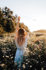 A girl in a dress stands with her back in a blooming field with daisies
