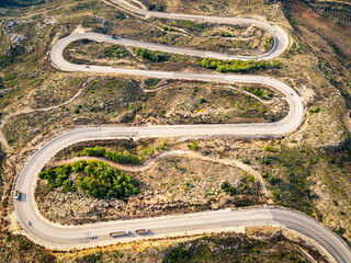 A winding asphalt road that passes through areas with few trees in autumn. An S-curved highway