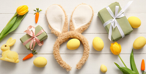 Bunny ears with Easter eggs, carrots, gift boxes and tulip flowers on white wooden background