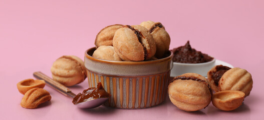 Bowl with sweet walnut shaped cookies with boiled condensed milk on pink background