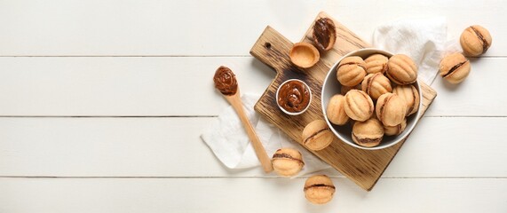 Composition of sweet walnut shaped cookies with boiled condensed milk on white wooden background with space for text, top view