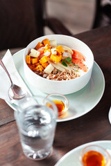 A healthy granola bowl with yogurt, mango, papaya, banana, honey, coconut flakes, and flax seeds. Served with a glass of water and a cup of coffee, creating a perfect balanced breakfast