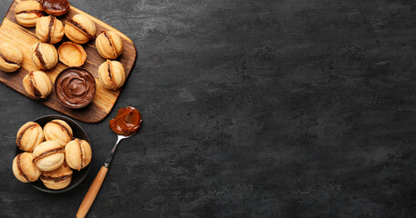 Wooden board and bowl of sweet walnut shaped cookies with boiled condensed milk on black background