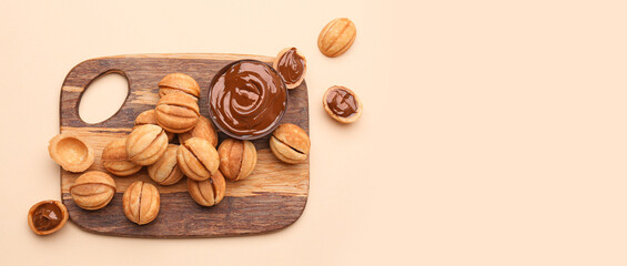 Wooden board of sweet walnut shaped cookies with boiled condensed milk on beige background