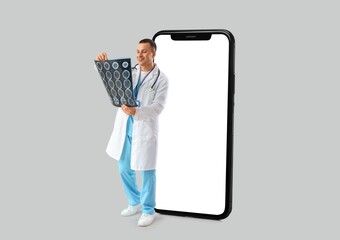 Male doctor with MRI scan and big smartphone on light background