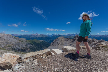 Young woman in sunglasses with hair blowing in the wind looking at the sky in front of an awesome panorama in the Dolomites, Mount Latemar, Trentino, Italy. Outdoor sport activity concept