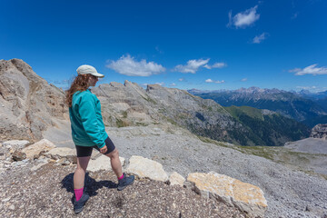 Young woman in sunglasses and sport clothes looking at the awesome summer panorama in the Dolomites, Mount Latemar, Trentino, Italy. Traveling photography and outdoor sport activity concept