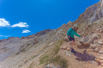 Young woman with long air and cap walking in the middle of dolomite peaks. Scenic landscape on the nature, Mount Latemar, Trentino, Italy. Traveling photography and outdoor sport activity concept