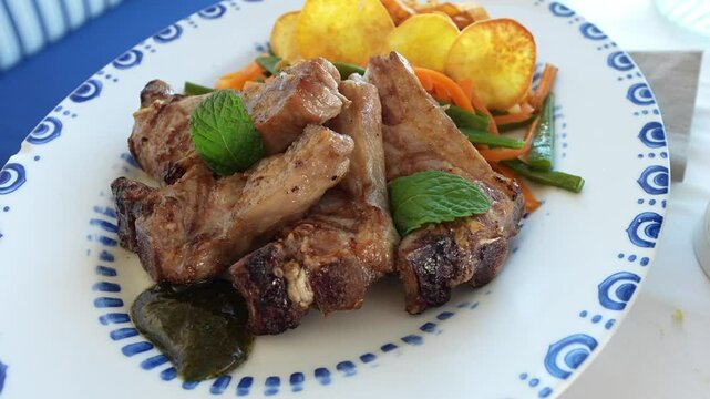 Close-up of grilled lamb chops with mint leaves, sweet potato slices and vegetables on a blue-patterned plate, Algarve