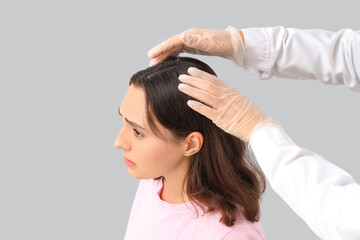 Trichologist examining young woman's scalp with dandruff on light background, closeup