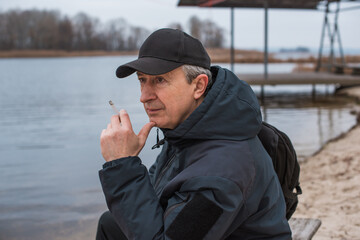 Obraz premium Older man, a resident of a large metropolis, leads an unhealthy lifestyle, siting and smokes cigarettes in park