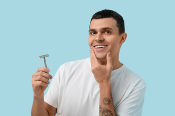 Handsome young man with razor after shaving on blue background