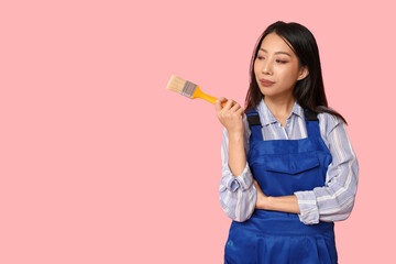 Female Asian thoughtful painter with brush on pink background