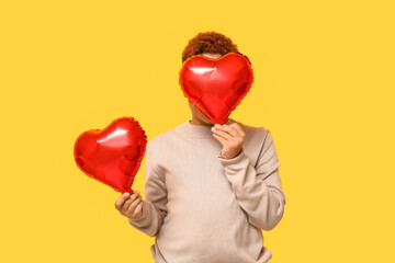 Cute little African-American boy with heart shaped air balloons on yellow background. Valentine's day celebration