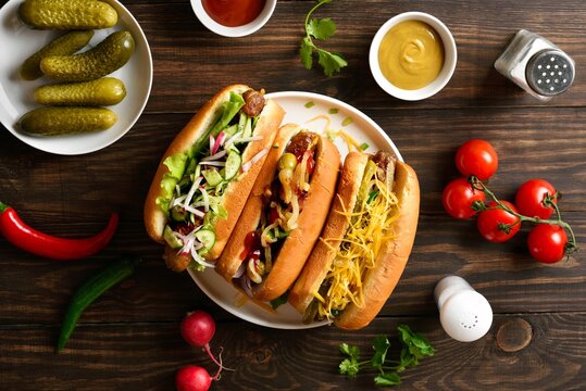 Hot dogs loaded with assorted toppings on wooden background